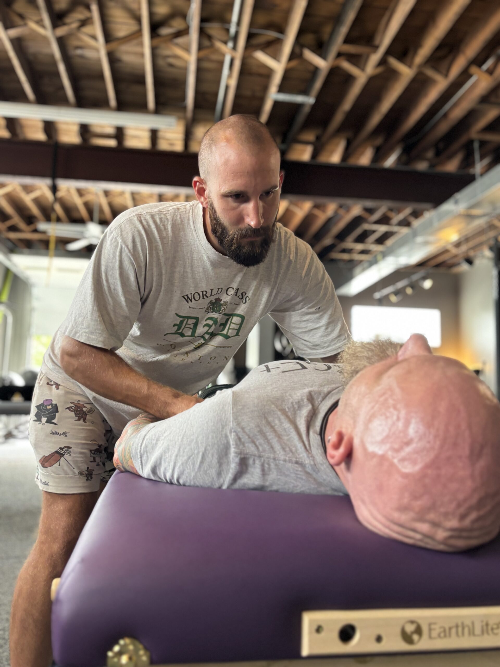 A person is receiving a therapeutic treatment while lying on a massage table, as another individual performs a technique at their head.